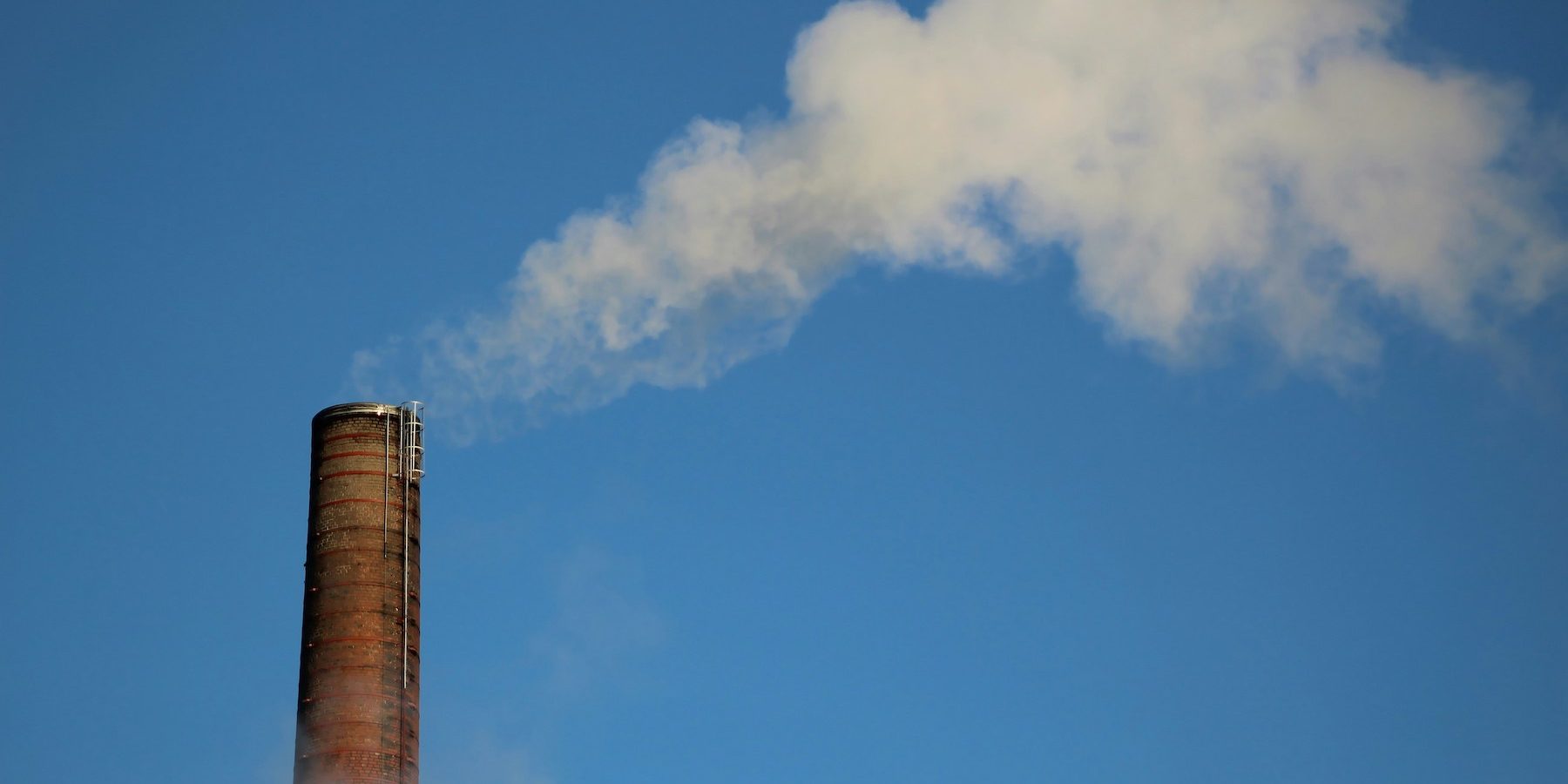 Single smoke stack emitting smoke against a blue sky