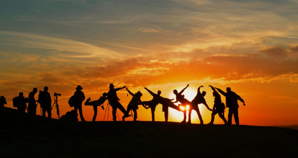 A group of people join together on a mountain top at sunset to take photos.